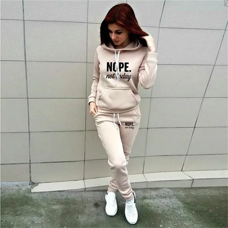 Woman wearing a beige tracksuit set featuring a hooded sweatshirt and joggers with "NOPE. not today" slogan print.