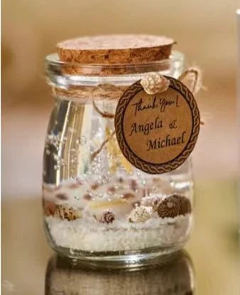 Glass jar favor with beach sand and seashells, topped with a cork stopper and a rustic "Thank You" gift tag.