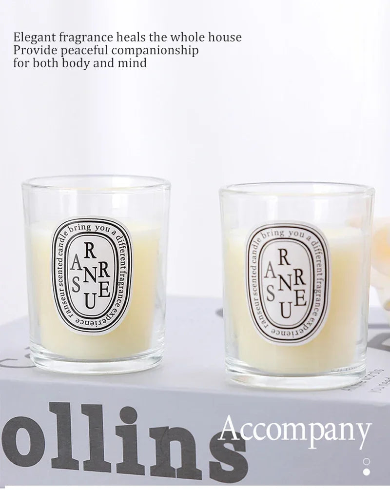 Two scented candles in clear glass tumblers with minimalist oval labels and off-white wax, resting on a white surface.