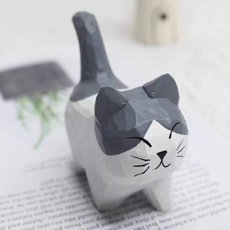 Small hand-carved wooden cat ornament in grey and white with a playful, faceted finish.