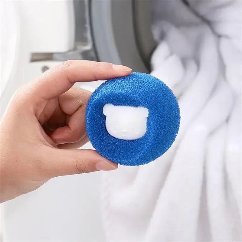Hand holding a round, blue laundry sponge with a white bear-shaped centre, in front of a washing machine.