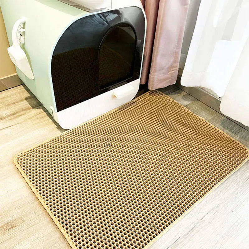 Beige double-layer honeycomb cat litter mat on a wooden floor in front of a modern mint green litter box.