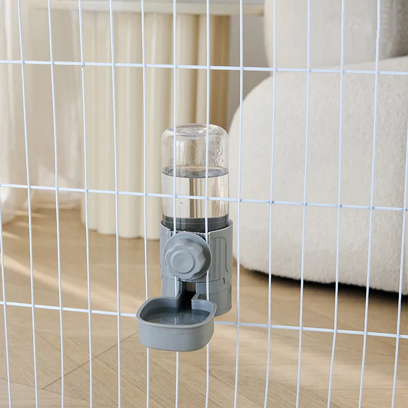 Grey plastic pet water dispenser mounted on a white wire cage, featuring a clear bottle and a small drinking bowl.