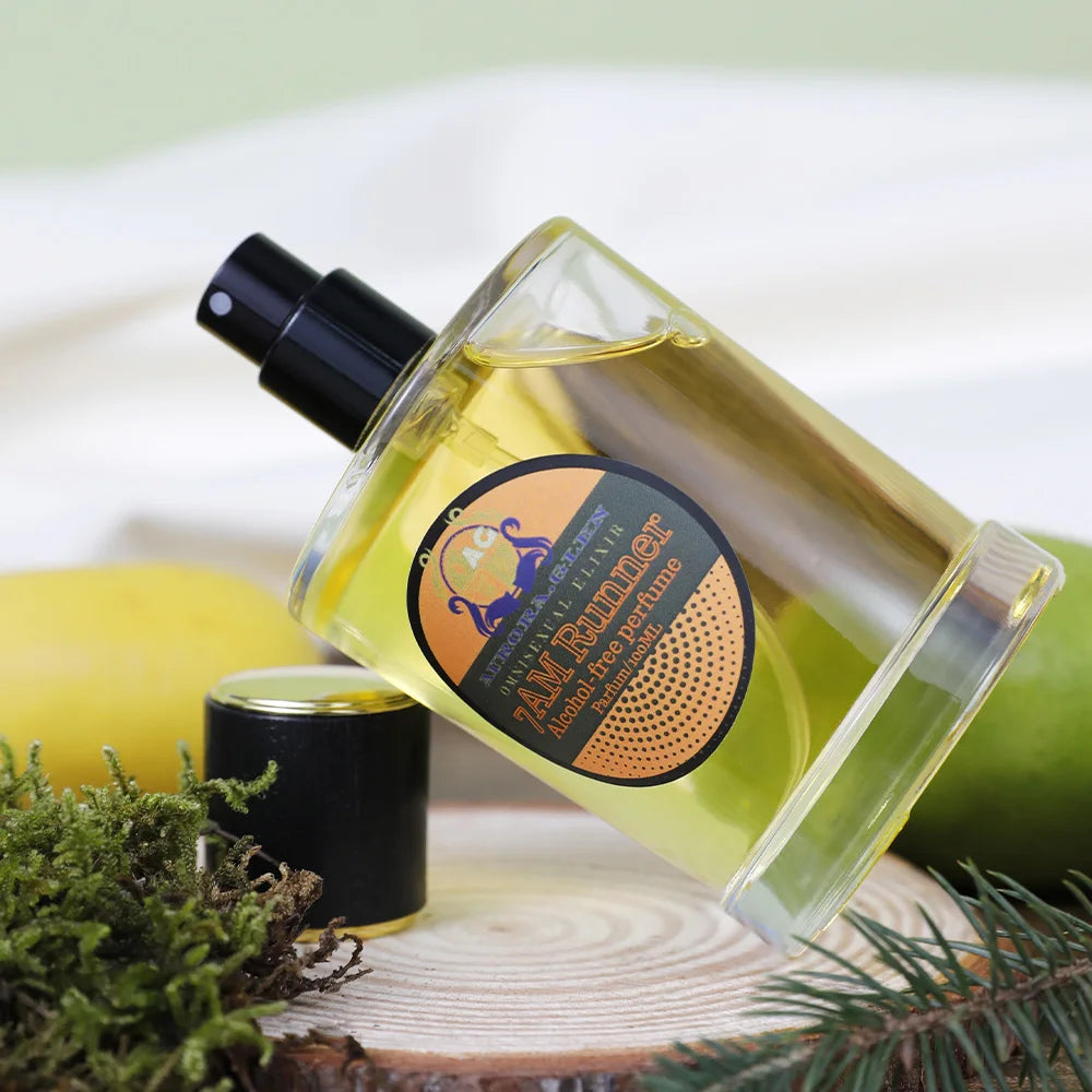 A 100ml bottle of yellow alcohol-free perfume with a black cap, displayed on a wooden slice with moss and citrus.