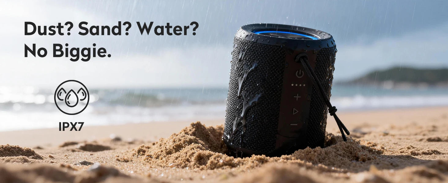 Black waterproof portable Bluetooth speaker in sand, featuring tactile buttons, a carry cord, and IPX7 rating.