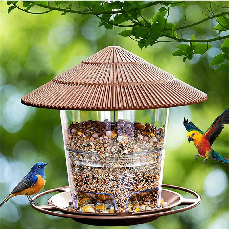 Hanging bird feeder with a brown ridged roof, clear seed reservoir, and circular perch, set in a garden.