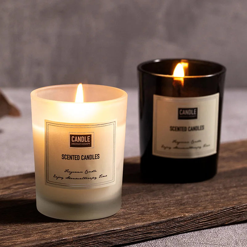 Two burning scented candles in black and frosted glass holders on a wooden base.