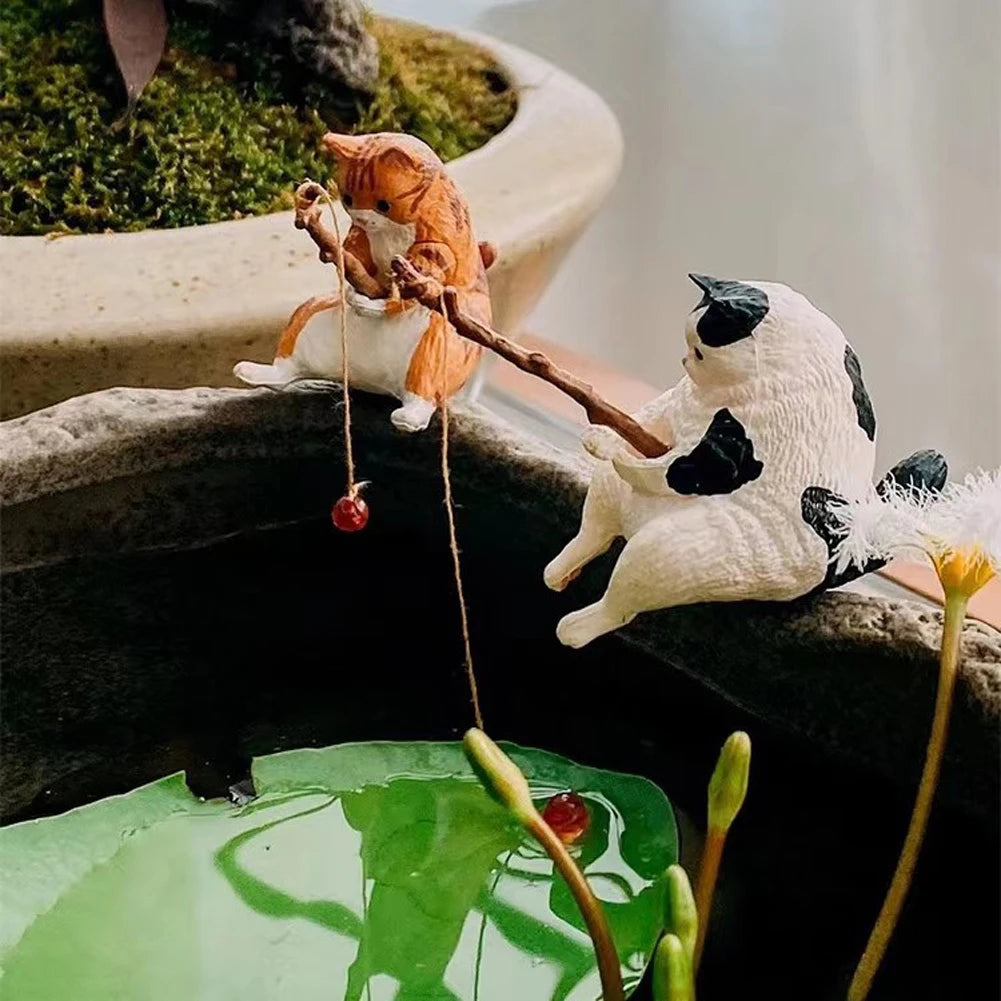 Two cute cat figurines, one ginger and one white with black spots, sitting on a stone edge, fishing with rods.