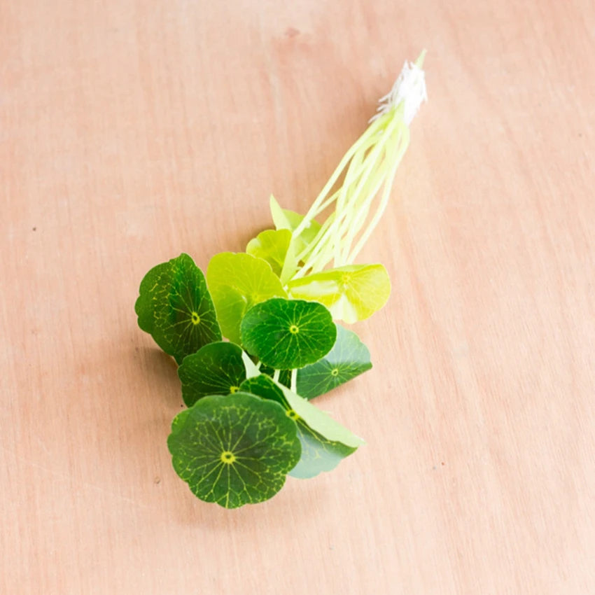 Artificial lotus plant with round, green leaves and long stems on a light wooden background.