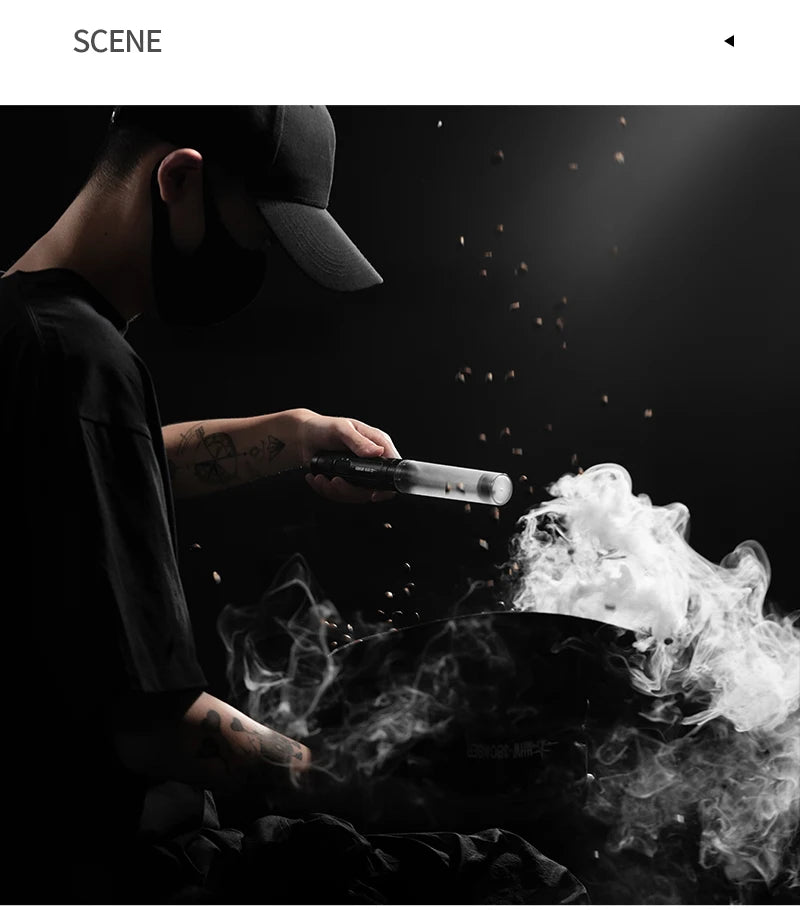 A person in black clothing uses a handheld, cylindrical smoking infuser to add smoke to coffee beans.