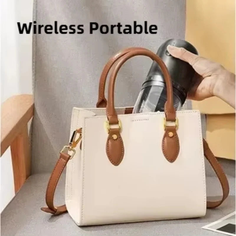 A hand places a black wireless portable blender into a cream-colored handbag with brown handles and gold hardware.