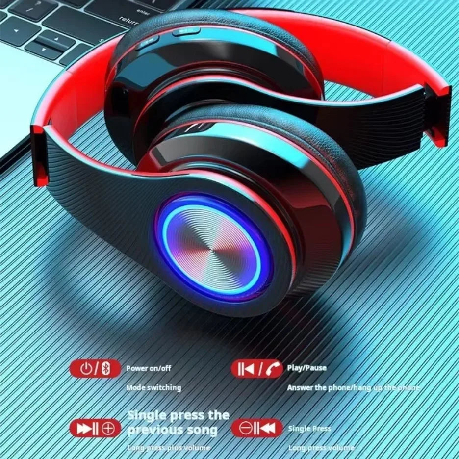 Wireless gaming headset in black and red with glowing LED ear cups, resting on a desk with button control diagrams.