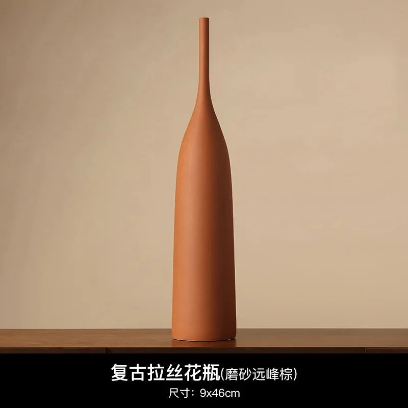 Tall, slender handmade ceramic vase in a rustic terracotta colour with a minimalist, Wabi-Sabi aesthetic.