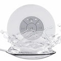 White circular waterproof Bluetooth speaker with a suction cup back and central media control buttons, splashing water.