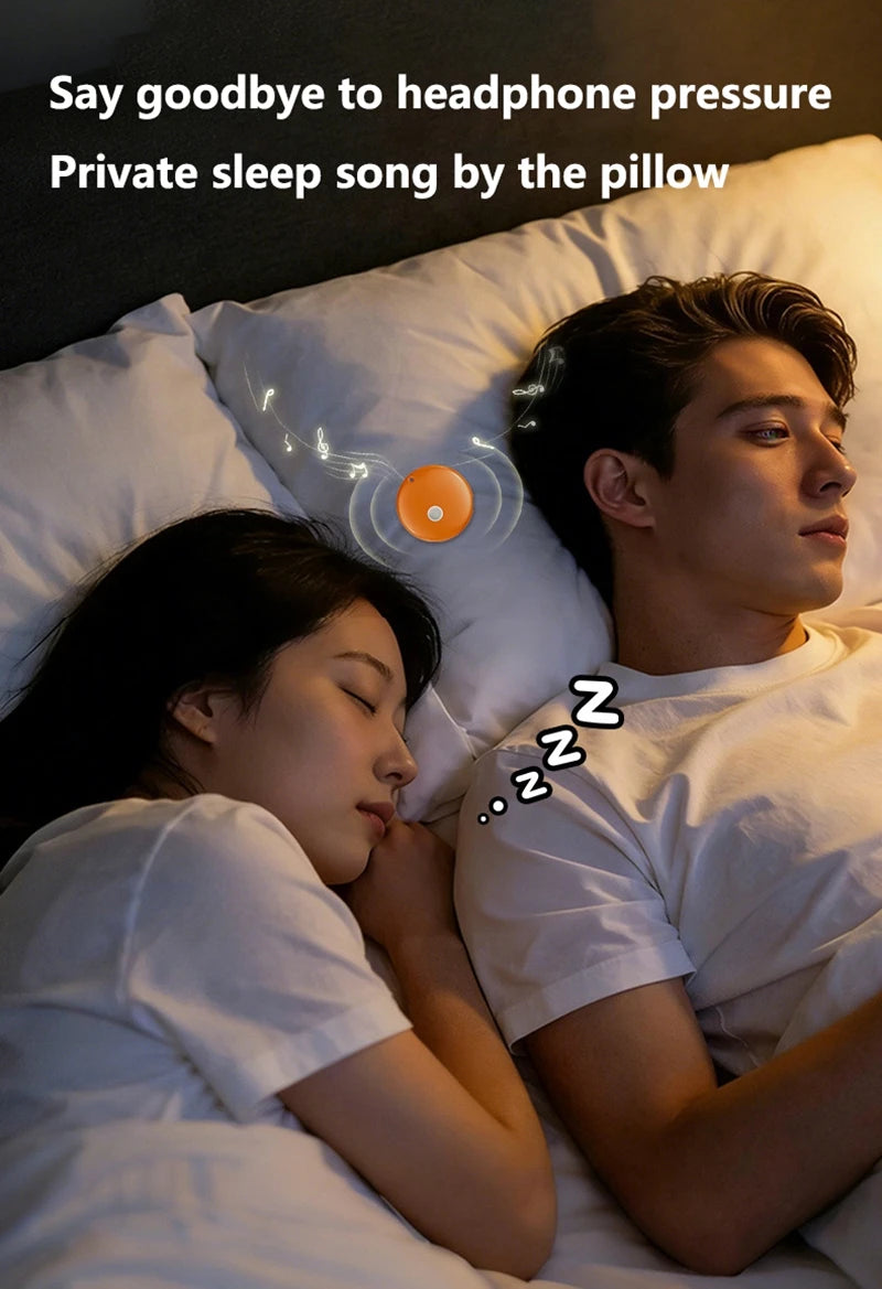 A small, orange circular Bluetooth speaker rests on a pillow between a sleeping couple, emitting musical notes.