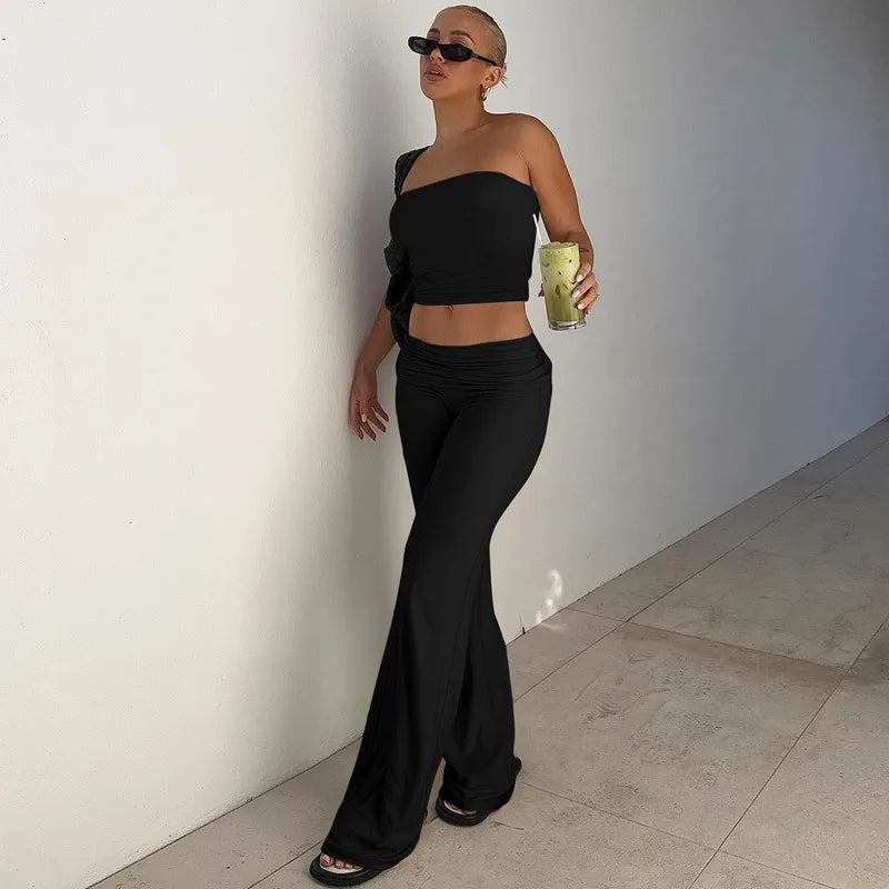 Woman wearing a black one-shoulder cropped top and high-waisted flared trousers against a white wall.