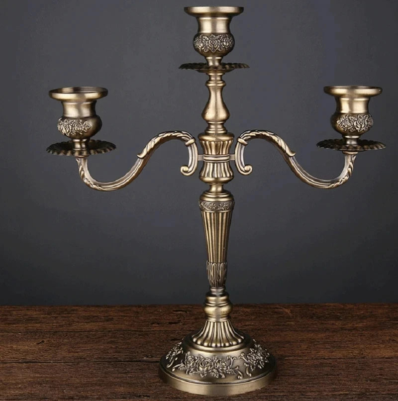 Bronze metal 3-arm candelabra with an ornate floral embossed design on a wooden surface.
