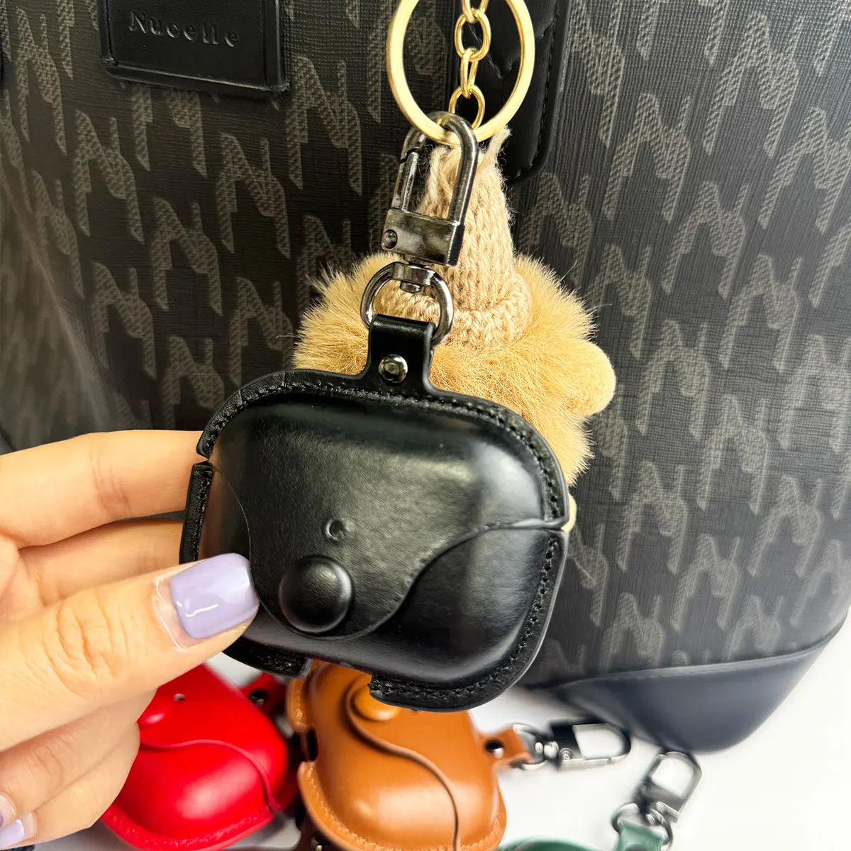 Black leather AirPods Pro case with snap button, key ring, and faux fur pom-pom attachment.