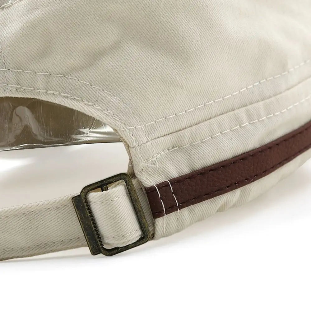 Close-up of a cream cadet baseball cap featuring a brown faux leather trim and an adjustable antique brass buckle strap.