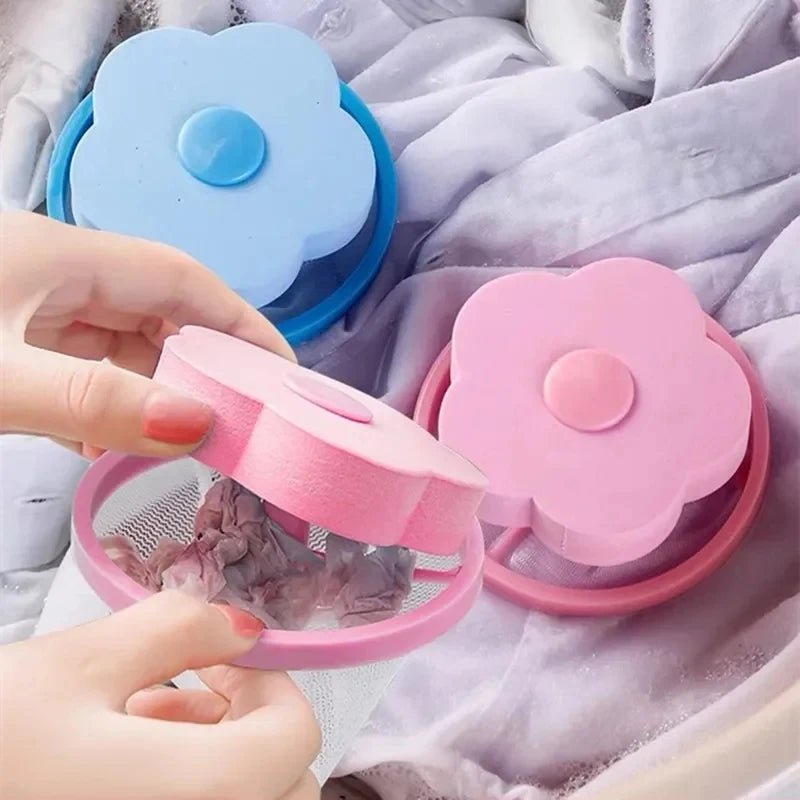 Hands holding a pink flower-shaped floating mesh laundry hair catcher with lint trapped inside, near a blue one.