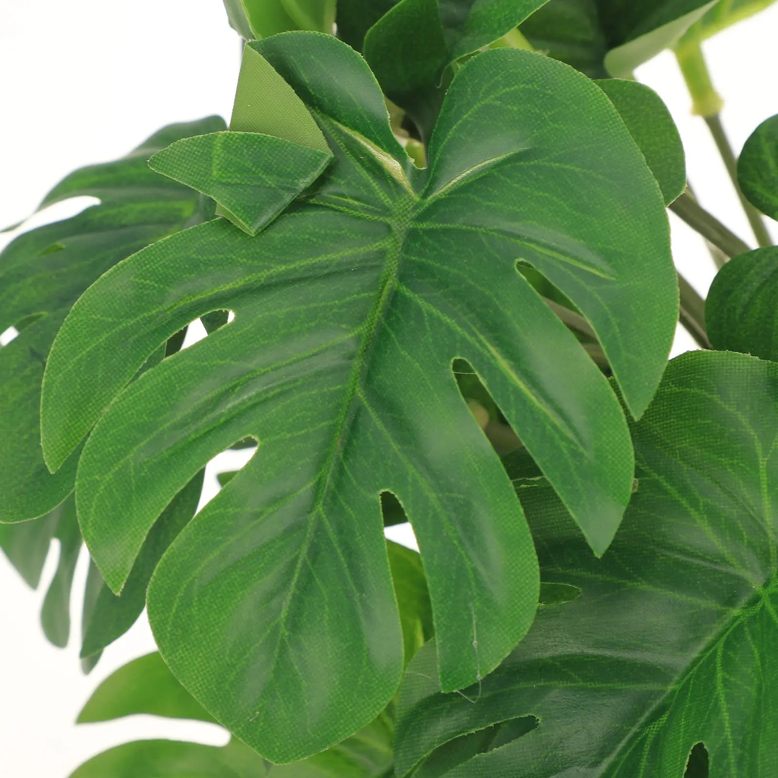 Close-up of artificial green monstera leaves for a terrarium, featuring realistic texture and split-leaf design.