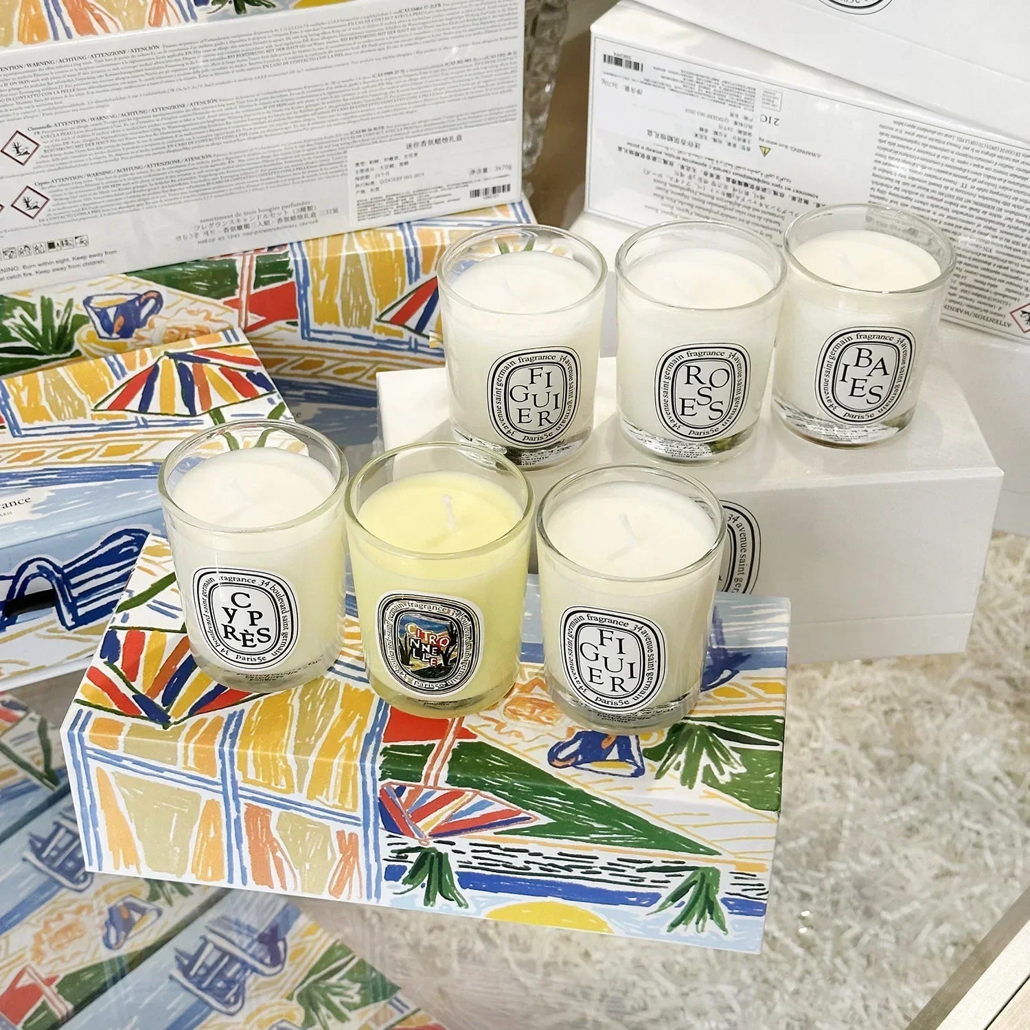 A set of five scented candles in clear glass tumblers with labels, presented in a colourful, illustrated gift box.