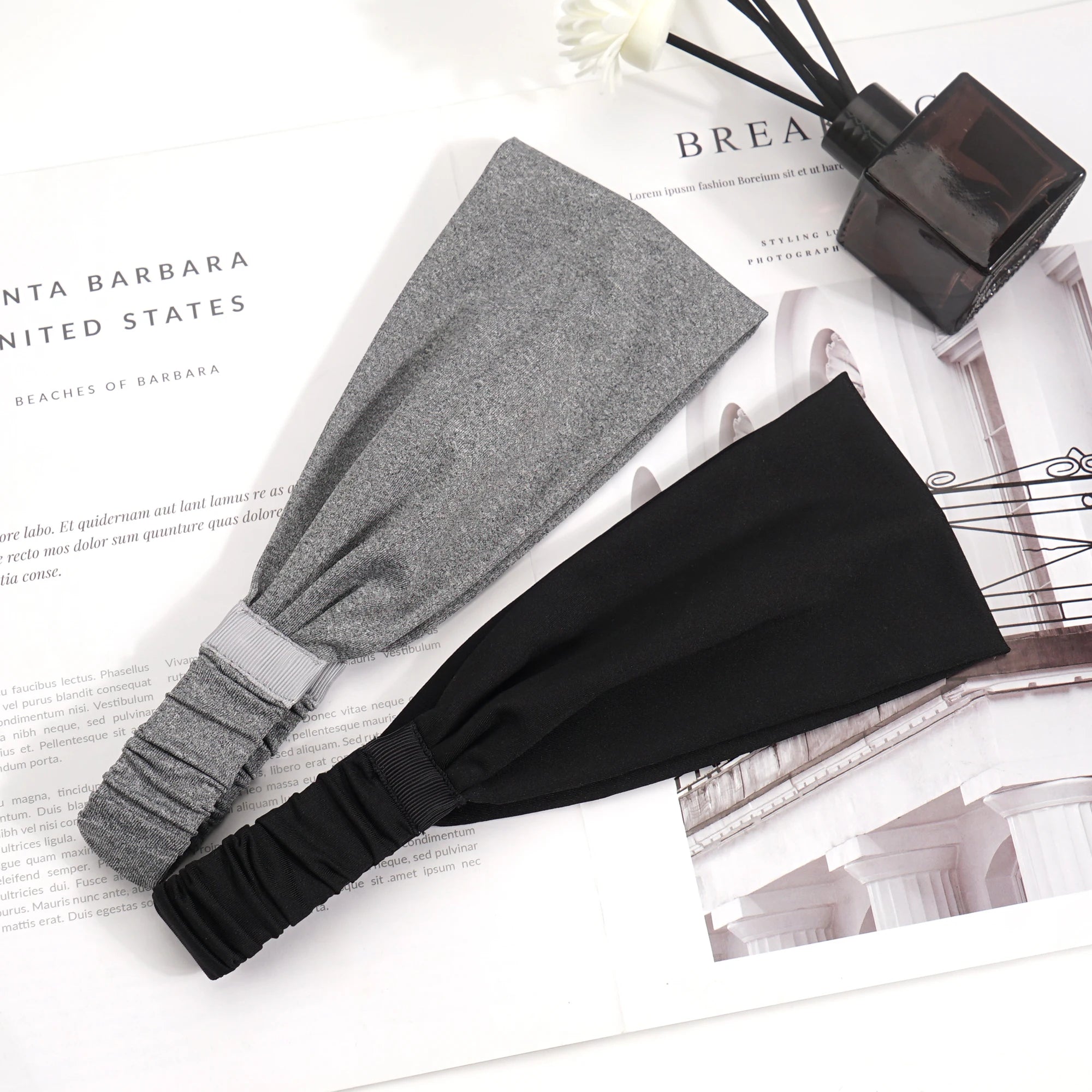 Two wide fabric headbands, one grey marl and one black, featuring an elasticated back section for a secure fit.