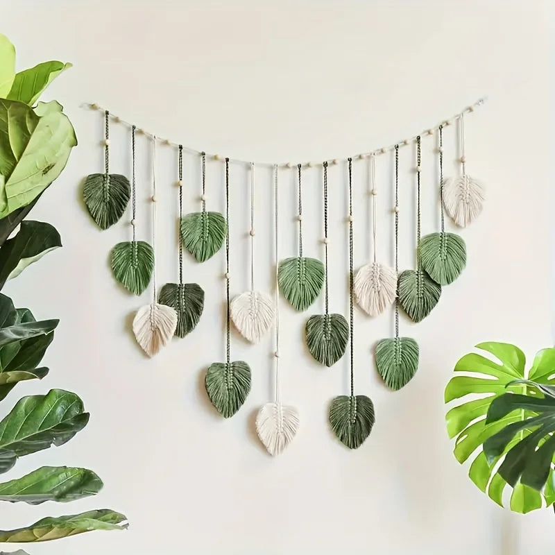 Boho macrame wall hanging featuring sage green and cream leaf-shaped pendants suspended on a beaded string.
