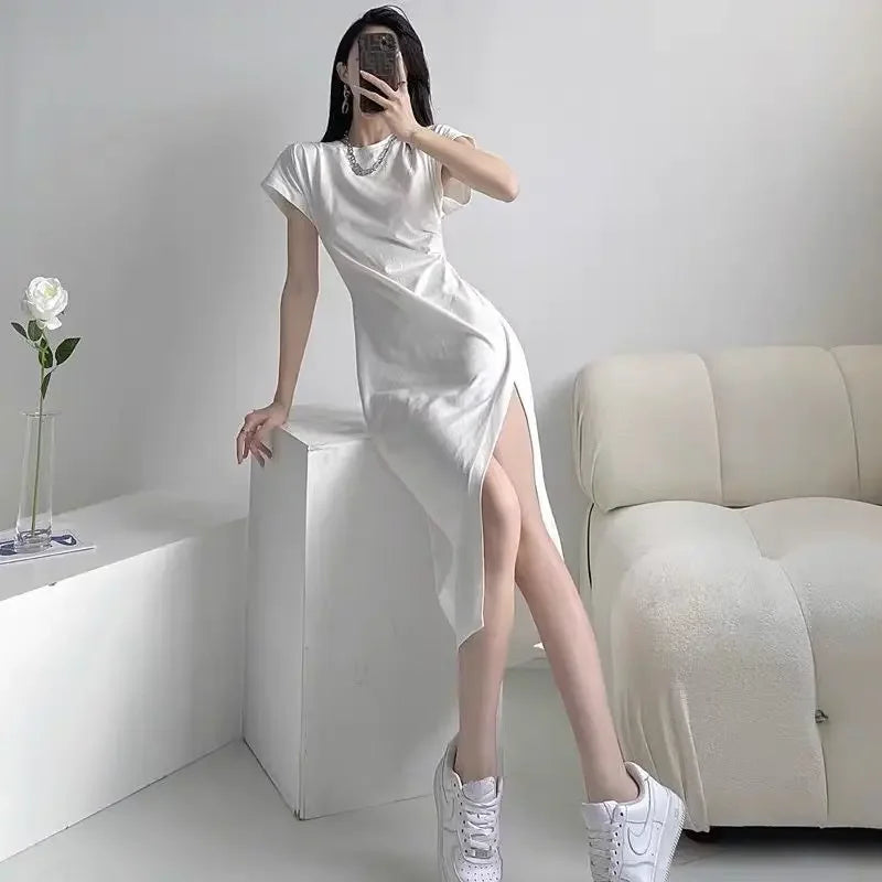 White short-sleeved midi dress with a high side slit, styled with trainers in a minimalist interior.