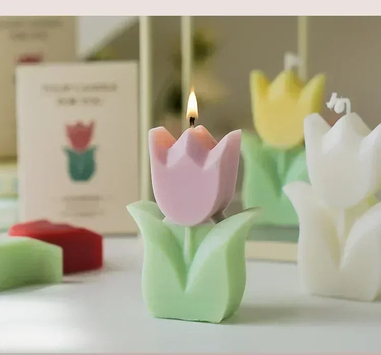A lit pink and green tulip-shaped candle with additional yellow and white tulip candles in the background.