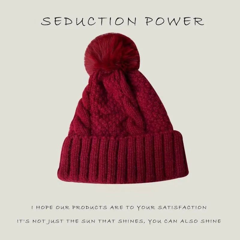 Deep red knitted beanie hat featuring a chunky cable knit design, a ribbed turn-up cuff and a matching pom-pom.