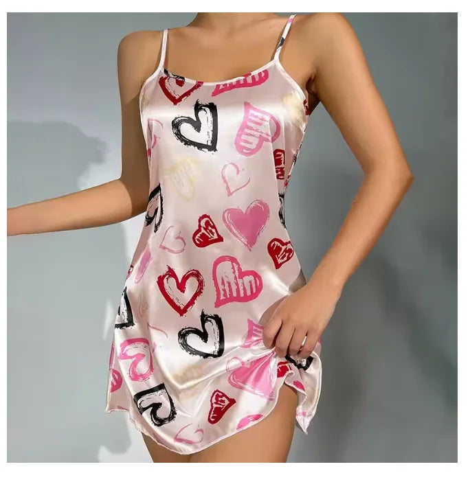Satin slip nightdress in pale pink with a multi-coloured heart print, featuring delicate spaghetti straps.