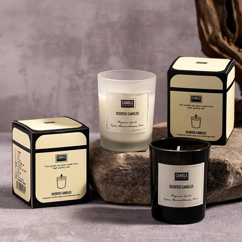 Two scented candles in frosted white and black glass jars, each with matching presentation boxes on a stone surface.
