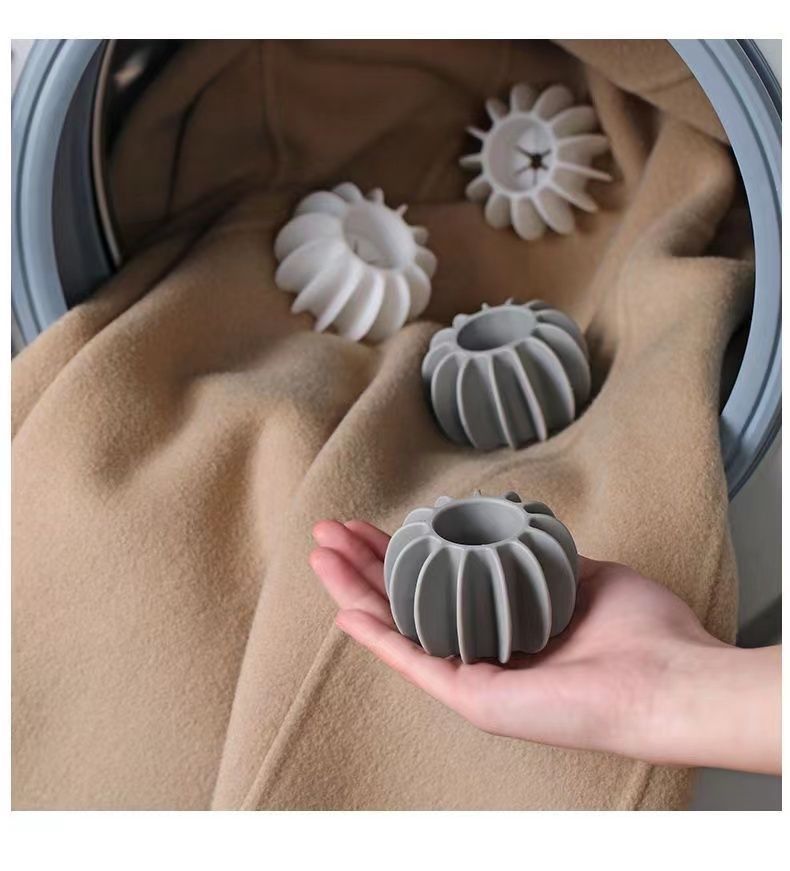 Hand holding a grey, ribbed silicone tumble dryer ball, with others inside a machine with beige laundry.