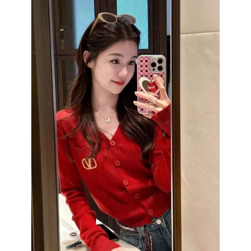 A woman wears a vibrant red button-up long-sleeve cardigan with a decorative gold embellishment on the pocket.
