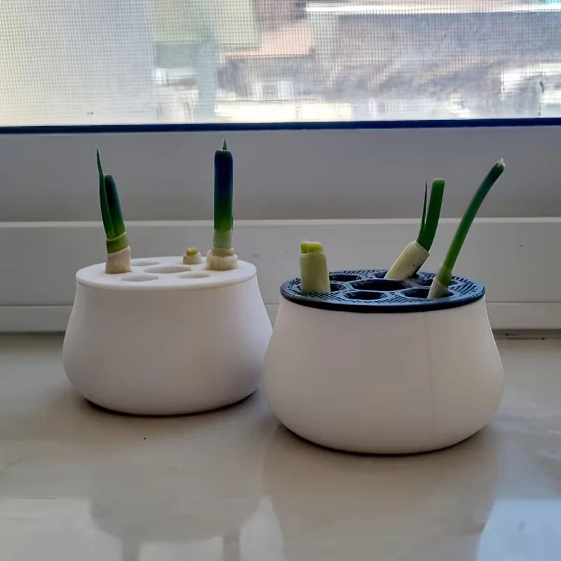 Two 3D-printed white hydroponic planters on a windowsill, each holding green onion scraps in a multi-hole lid.