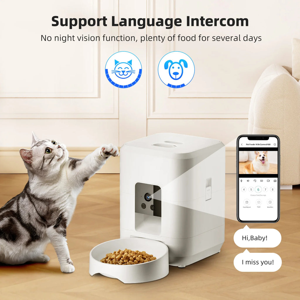A white, square automatic pet feeder with a camera, food bowl, and companion app interface shown on a smartphone.