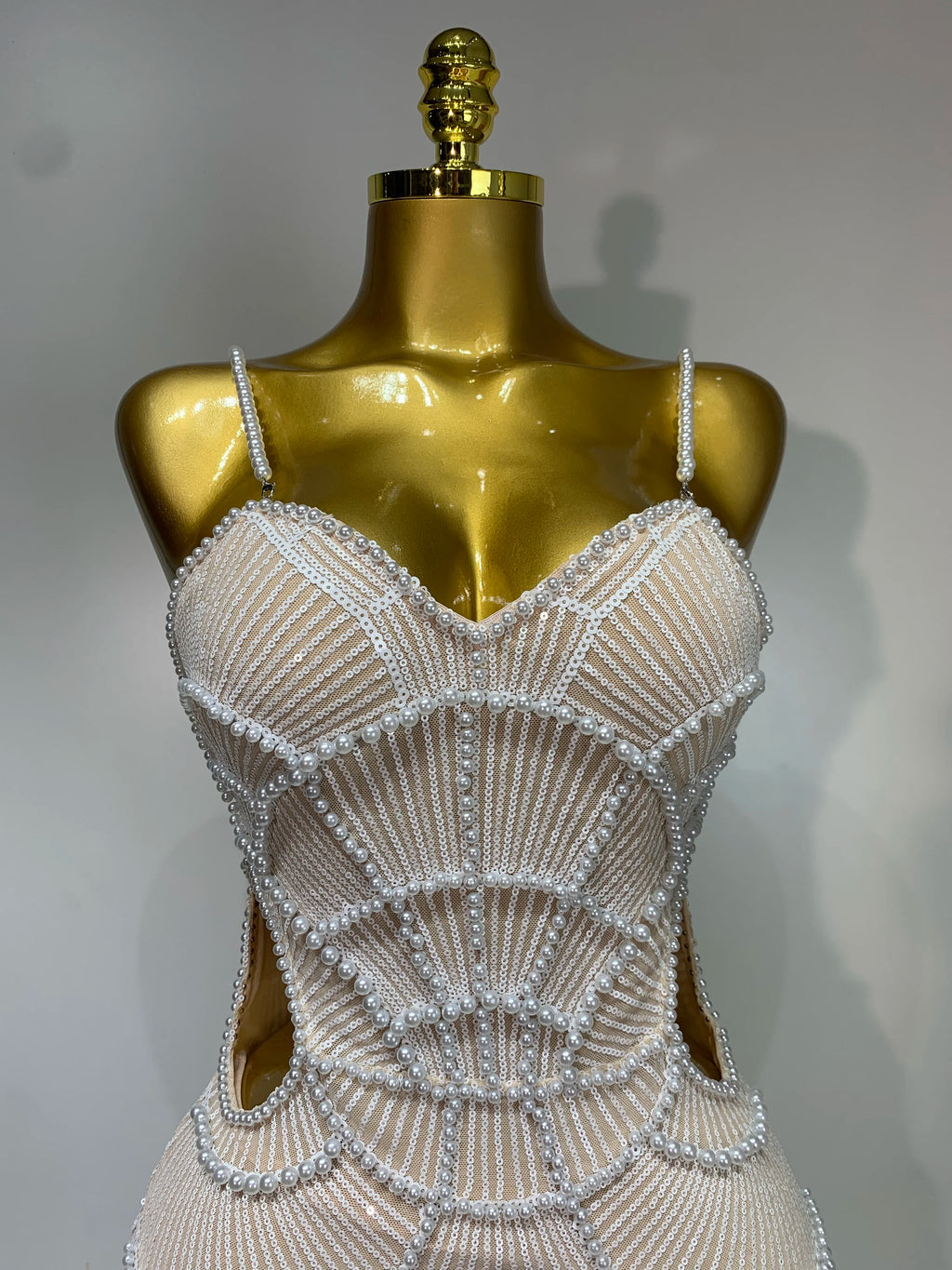 Beige V-neck bodycon dress with intricate white pearl beading and sequin details, displayed on a gold mannequin.