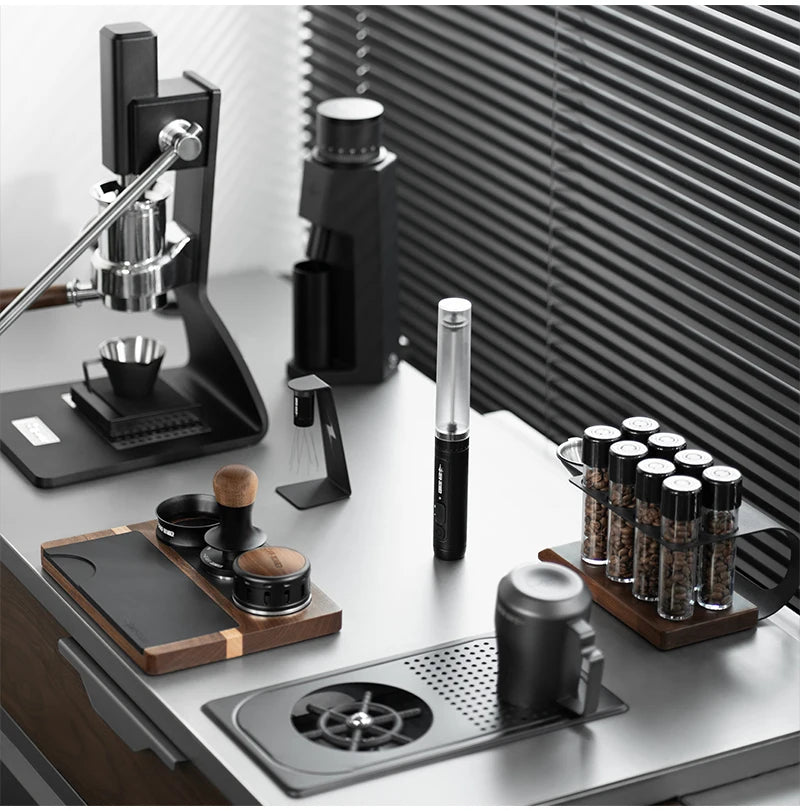 Minimalist espresso station with a black manual lever machine, grinder, glass bean tubes, and wood-accented accessories.
