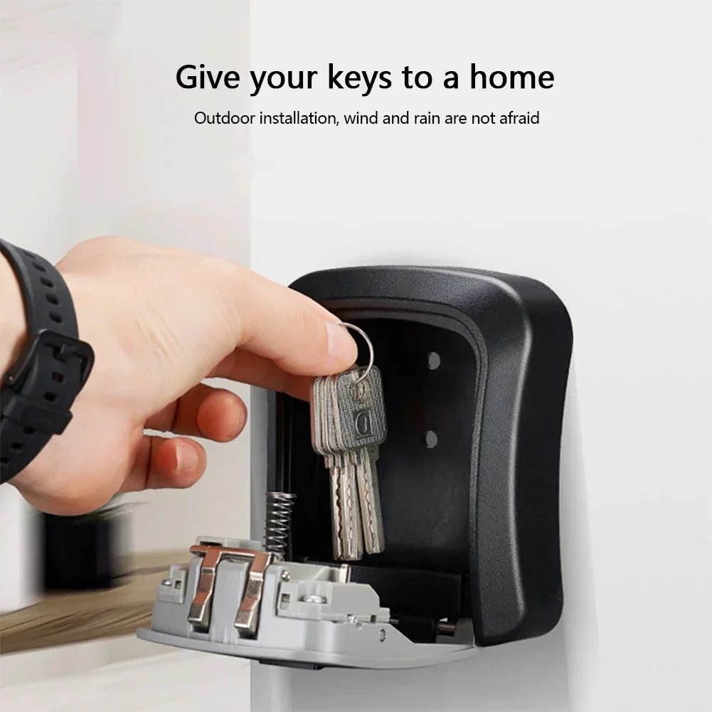 A black, wall-mounted metal key lock box with a hinged door, showing a hand placing keys inside.