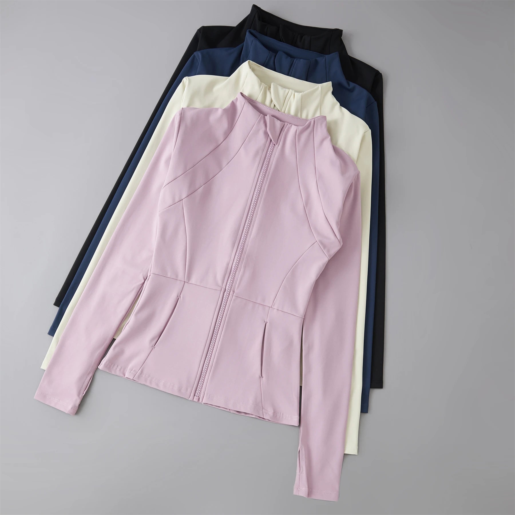 Stack of women’s zip-up sports jackets with high collars in pink, cream, navy, and black.