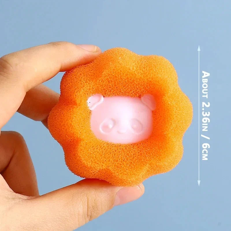 A hand holding a 6cm orange flower-shaped bath sponge with a cute pink panda character face in the centre.