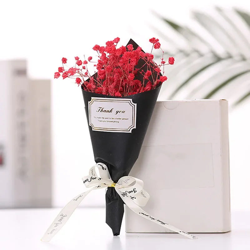 A bouquet of vibrant red artificial flowers wrapped in black paper with a white ribbon, featuring a 'Thank you' label.