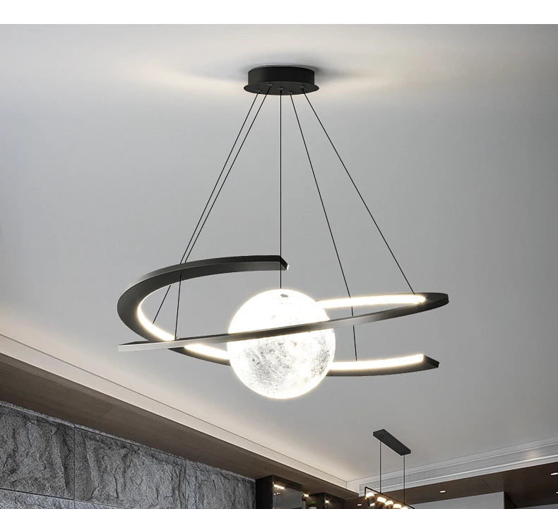 Modern black pendant light featuring a glowing, textured moon-like orb suspended within a sleek circular frame.