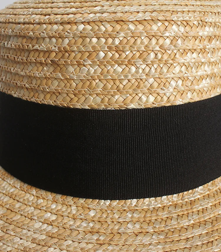 Elegant straw sun hat with a tightly woven texture and a wide, plain black ribbon band.