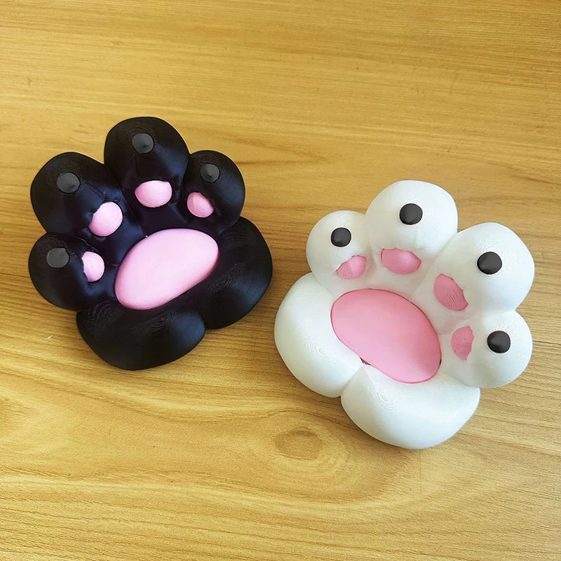 Two 3D-printed cat paw desk stands, one black and one white, featuring cute pink pads, on a wooden surface.