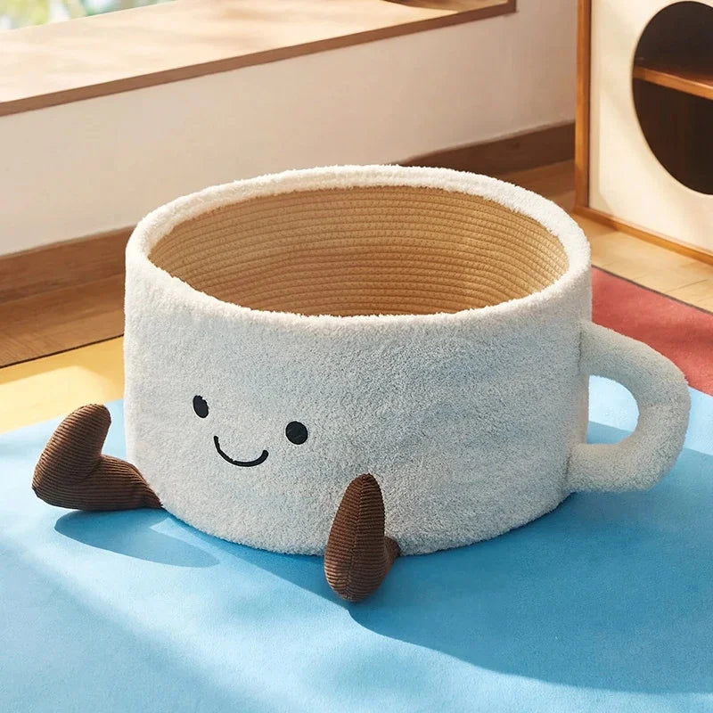 White coffee mug shaped cat bed with a smiling face, handle, and brown corduroy feet.