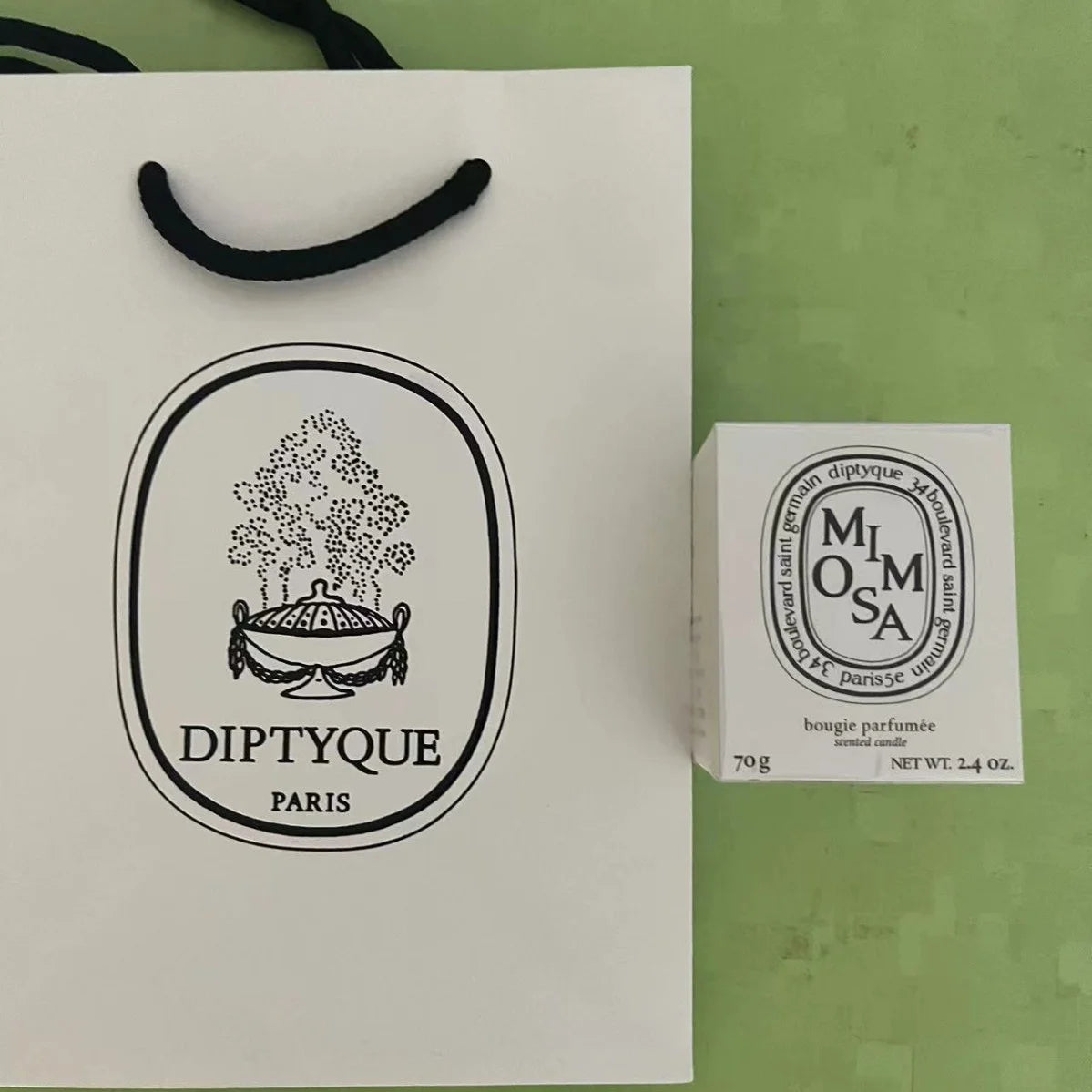 A small white scented candle box and a matching white paper gift bag with elegant black branding.