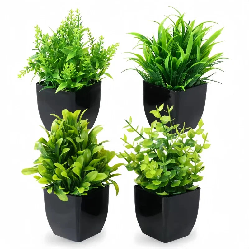 Four small, vibrant artificial green plants in square black pots, arranged in a grid against a white background.