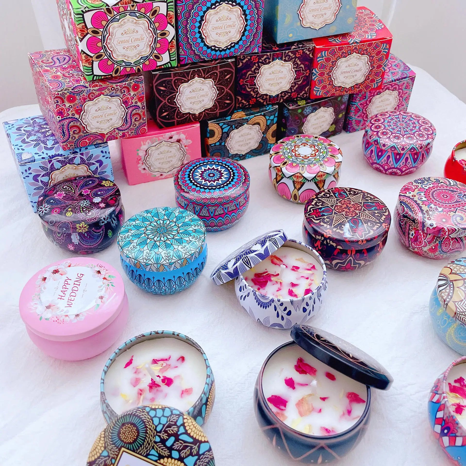 Assorted colourful scented candles in decorative metal tins and patterned boxes with floral wax designs.